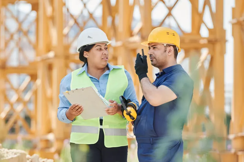 Two contractors in hard hats go over a project on site